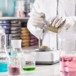 Medicine, pharmacy and cosmetology concept. Unrecognizable scientist manufacturing natural organic healthy cosmetics in laboratory, standing at desk with glass tubes filled with colored liquids